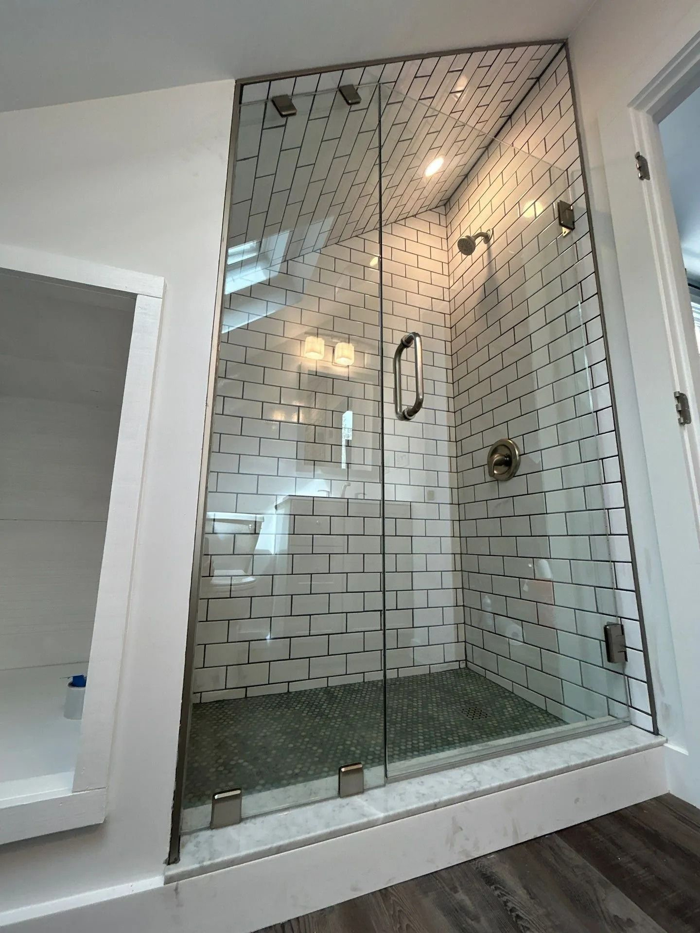 Glass walk-in shower with white subway tile and gray pebble floor in a bright bathroom.