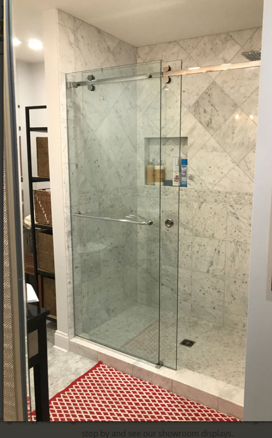 Glass shower enclosure with marble tile walls and red bath mat in a bathroom
