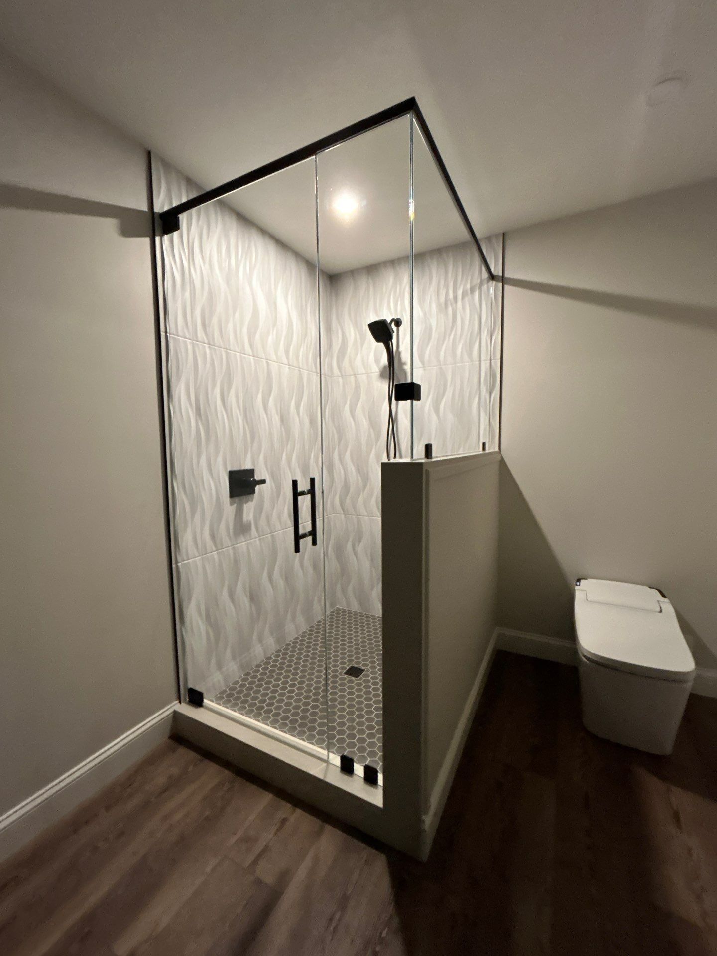 Modern bathroom with a glass shower stall, patterned tile, and a white toilet beside wood flooring