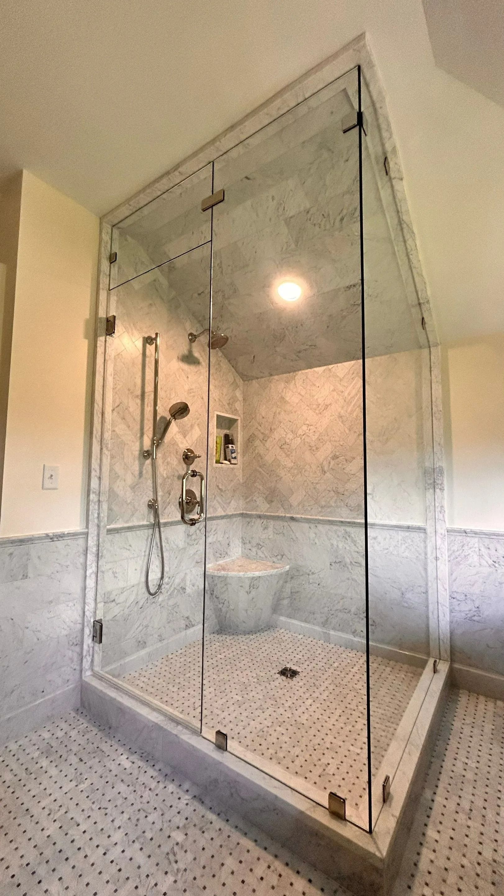 Glass-enclosed walk-in shower with tiled walls, handheld shower, and bench seat