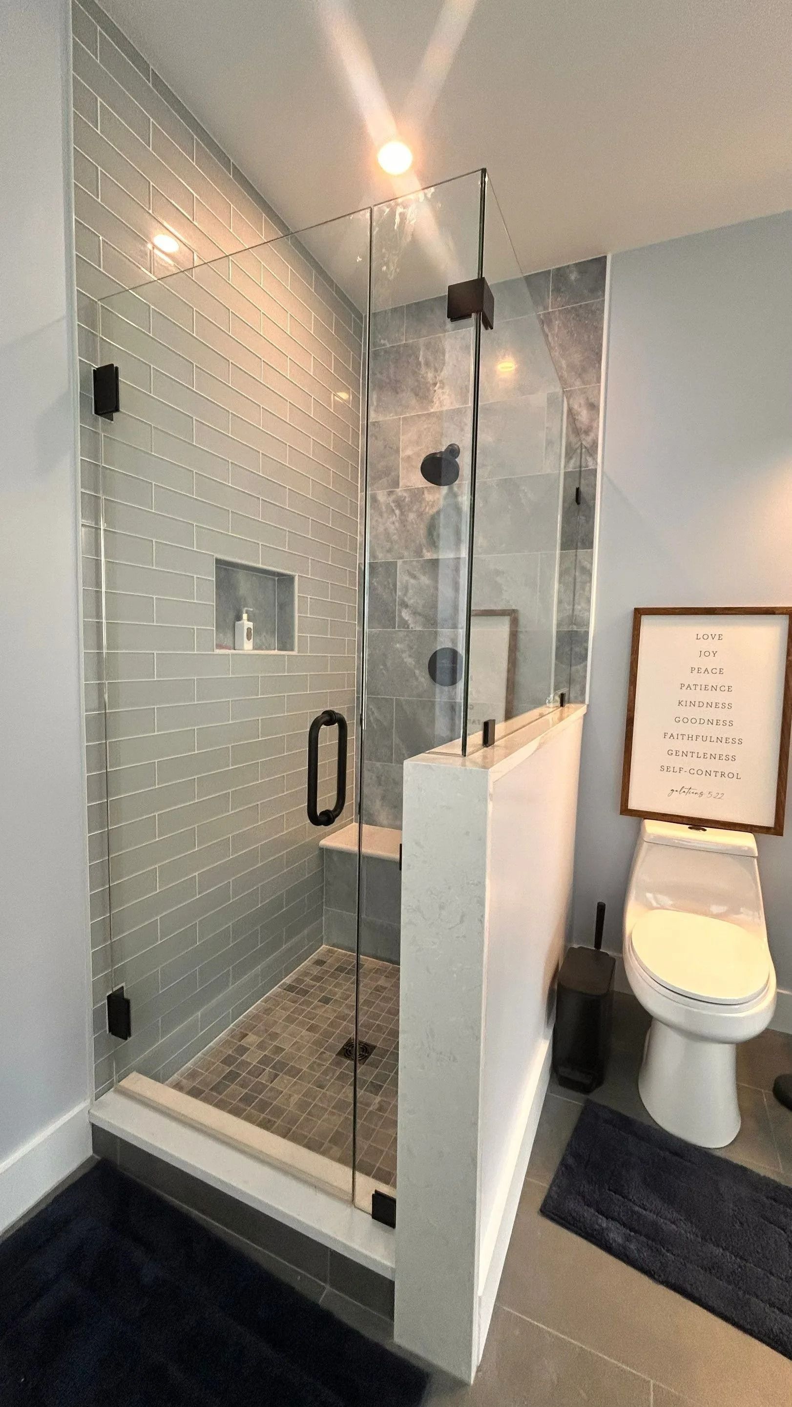 Glass shower stall beside a toilet in a modern bathroom, with gray tile and black fixtures