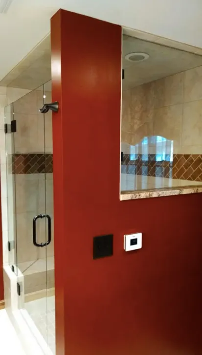 Red shower stall with glass door and beige tiled bathroom interior.