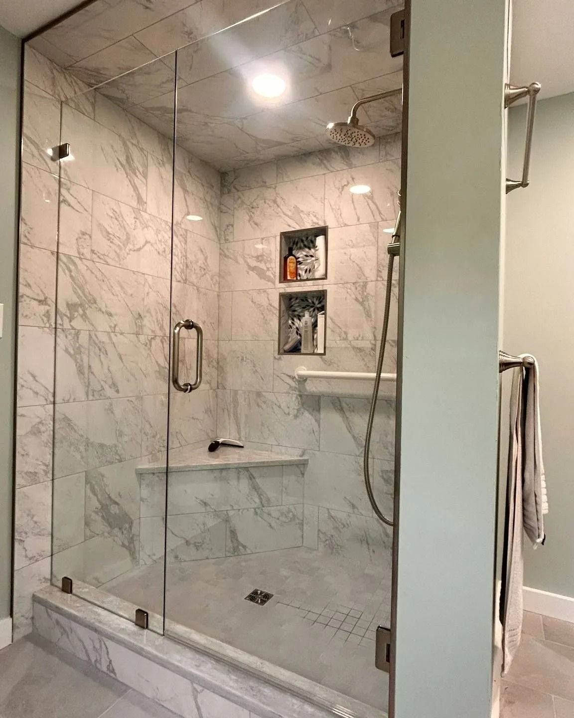 Glass-enclosed marble shower with chrome fixtures, built-in shelf, and towels hanging nearby.