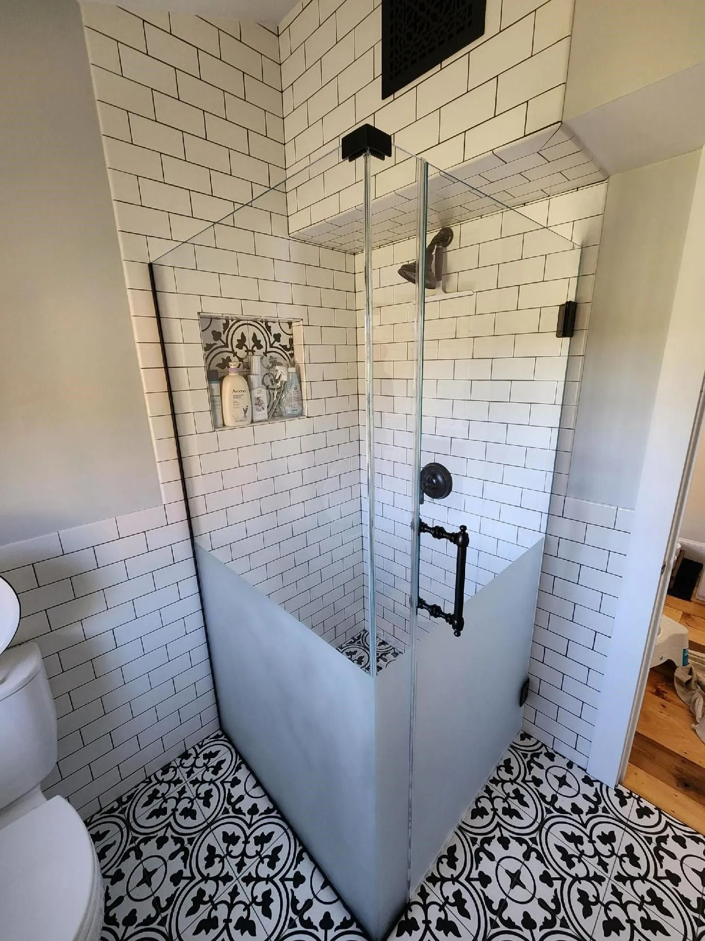 Corner glass shower with white subway tile and black-and-white patterned floor in a small bathroom