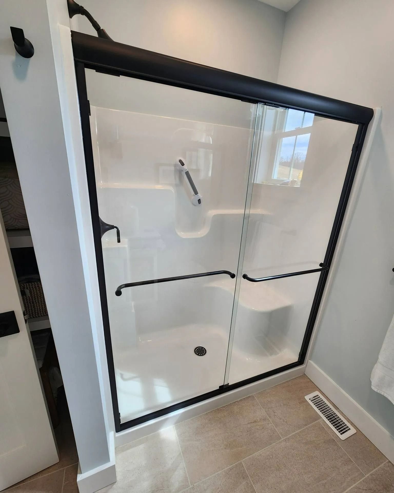 Glass shower enclosure with white walls and beige tile floor in a bathroom