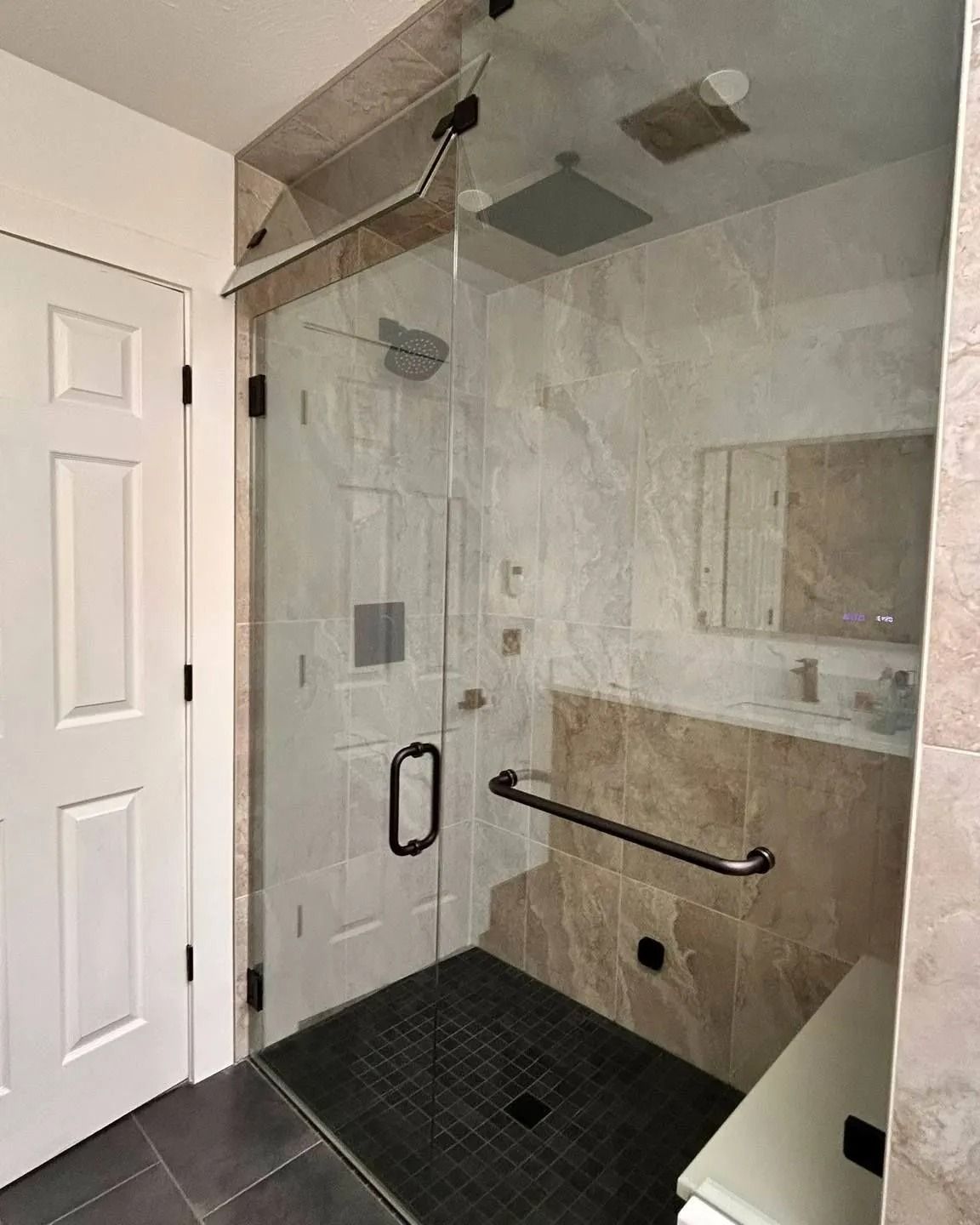 Accessible shower with grab bars, bench seat, handheld shower, and black tiled floor in a modern bathroom