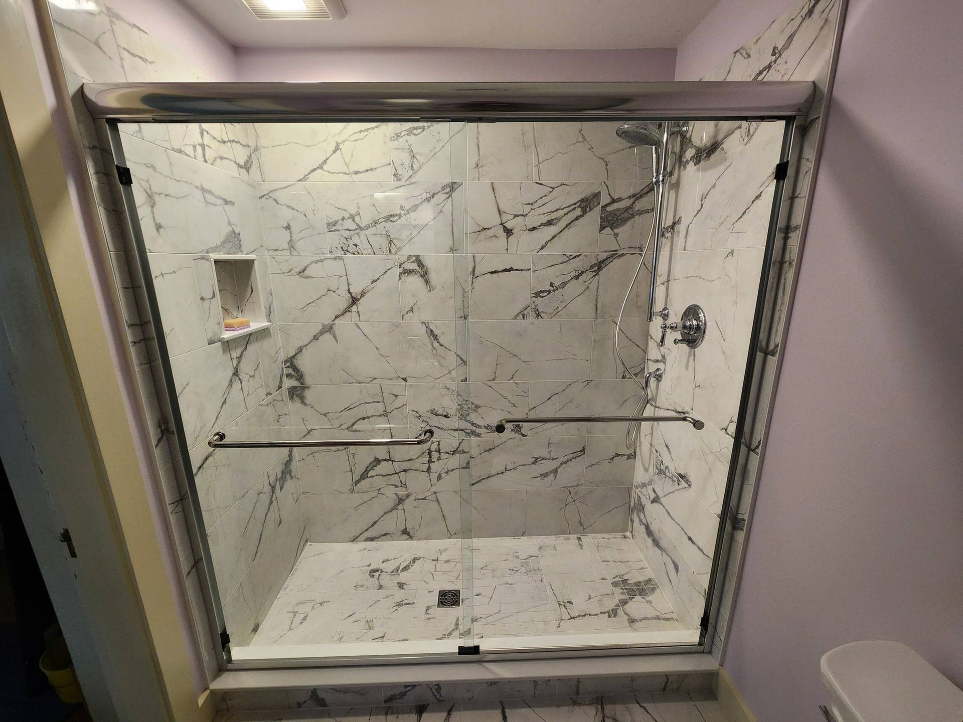 Empty walk-in shower with marble-patterned tile and glass door enclosure.