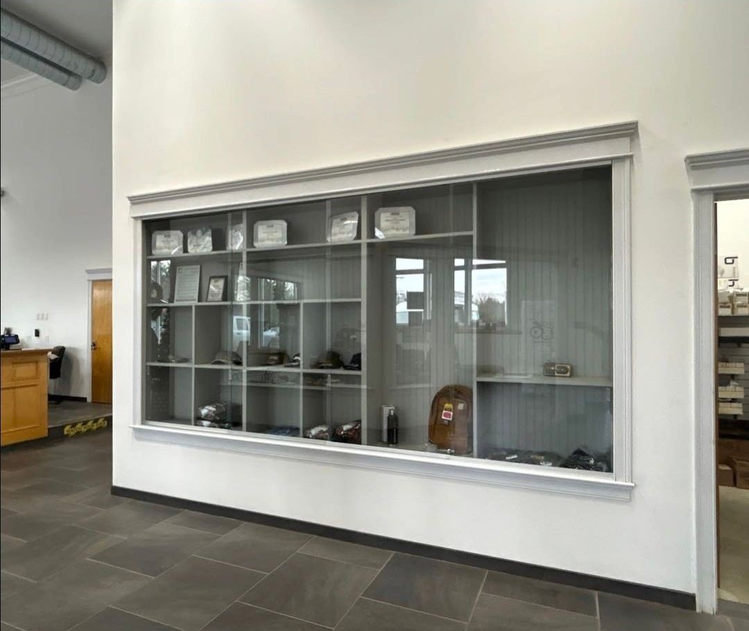 Office lobby display case with glass shelves, trophies, and decorative items against a white wall.