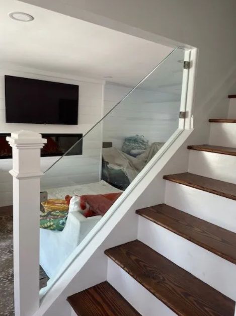 Staircase with dark wood treads and glass railing overlooking a bright living room with a wall-mounted TV.