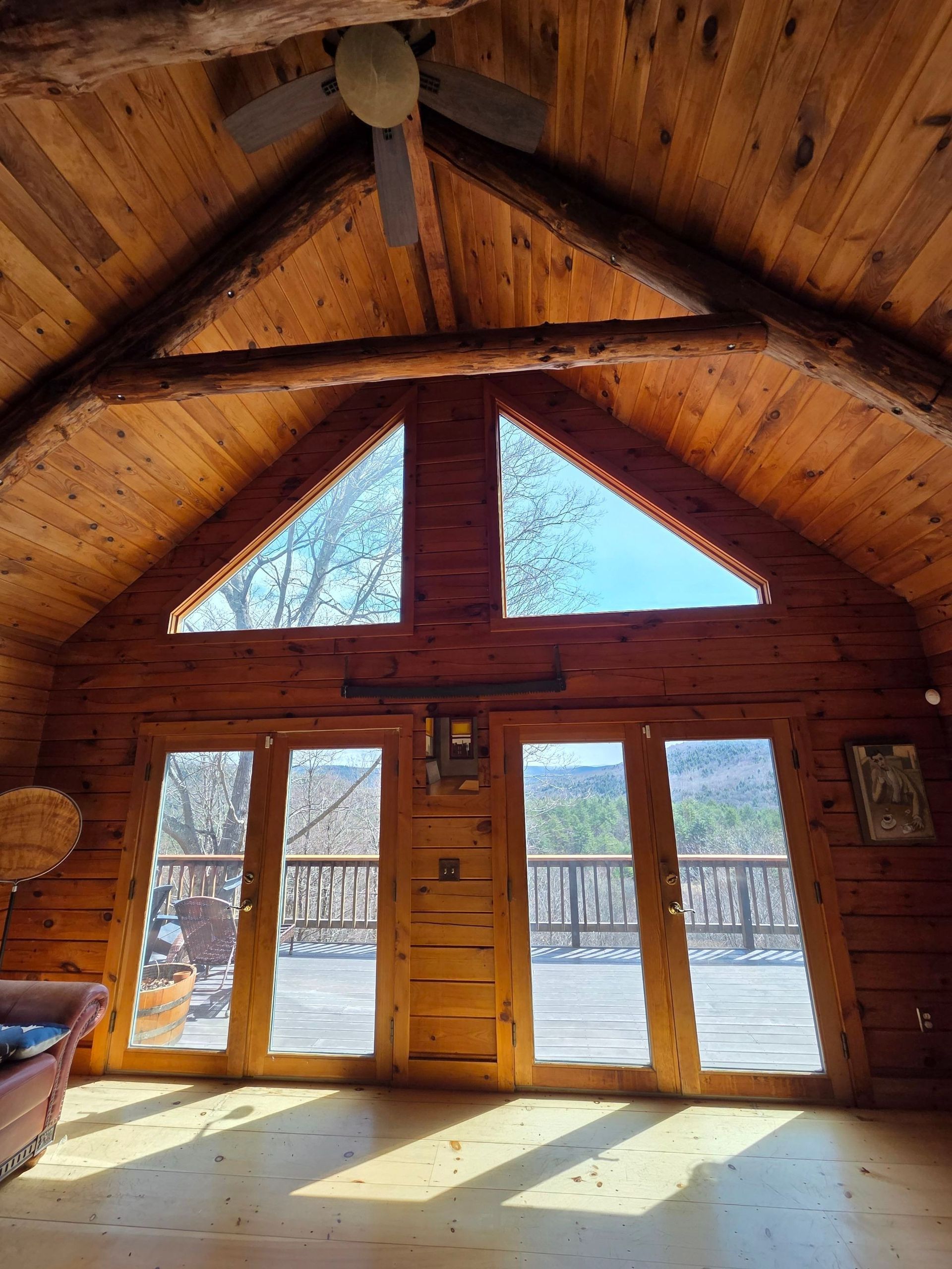 Sunlit log cabin interior with tall windows, wooden beams, and snowy trees outside