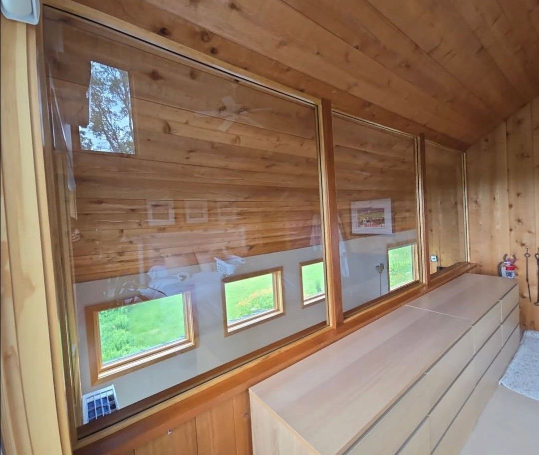 Wood-paneled room with long bench seating and narrow windows overlooking grass.
