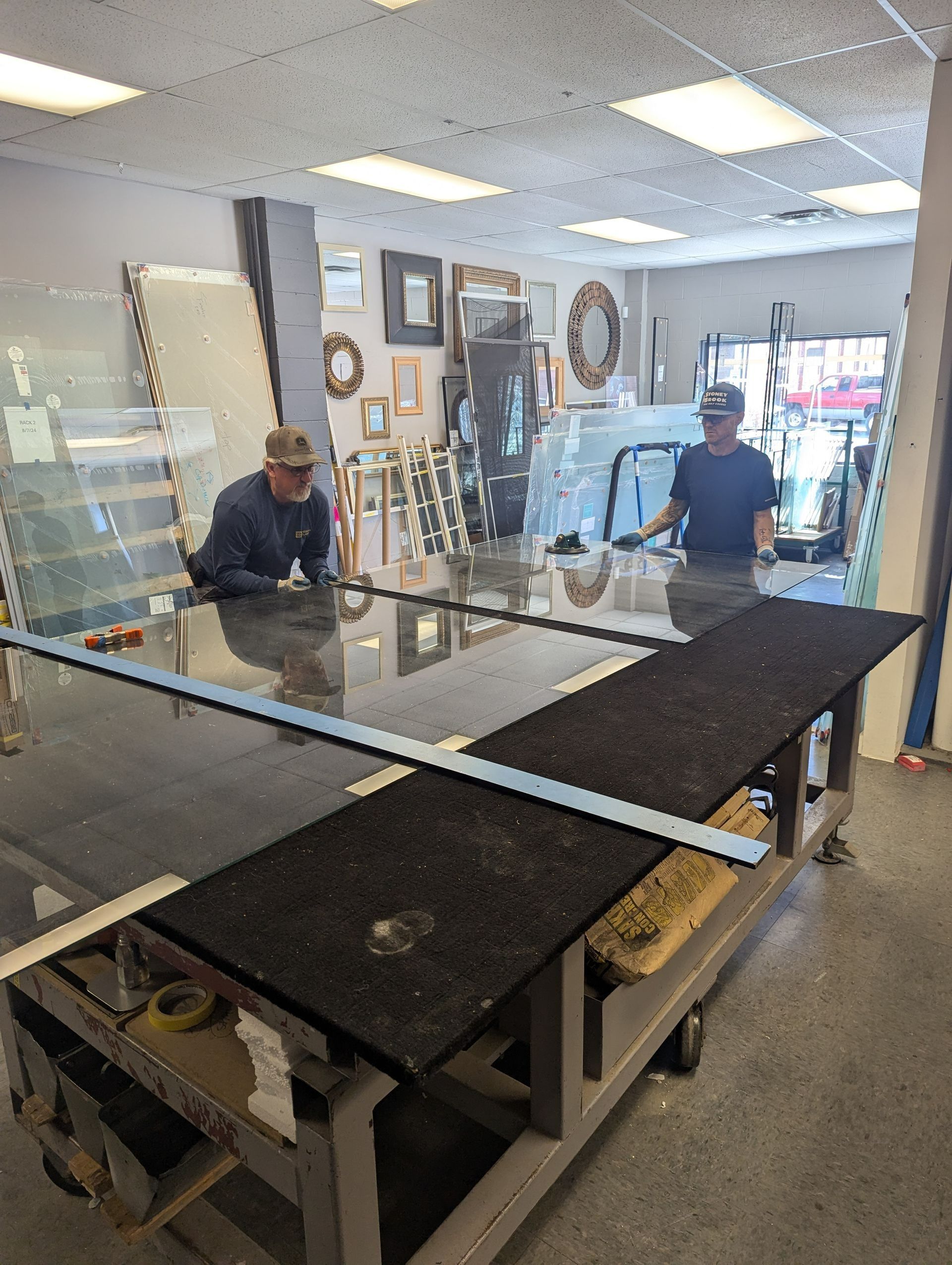 Two people assembling a large glass display table in a shop workshop.