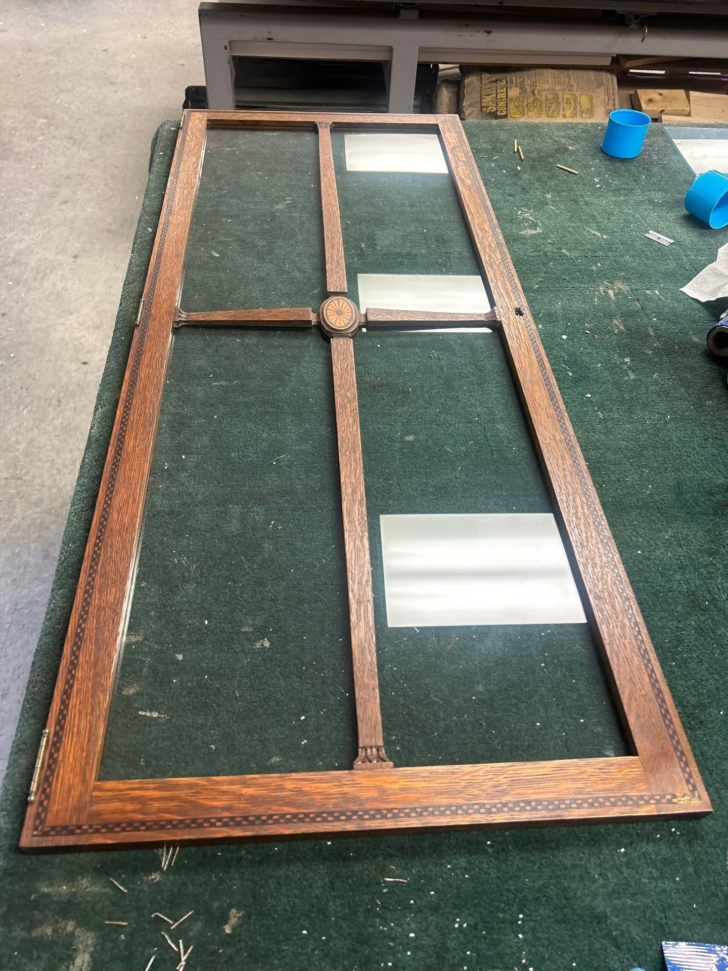 Wooden-framed glass door panel lying on the floor with a central round knob.