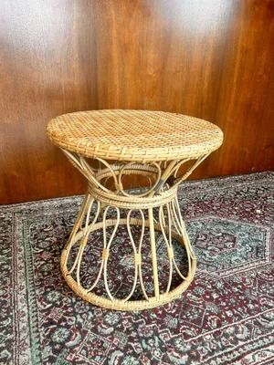 Woven wicker stool with round top on a patterned rug before a wood-paneled wall