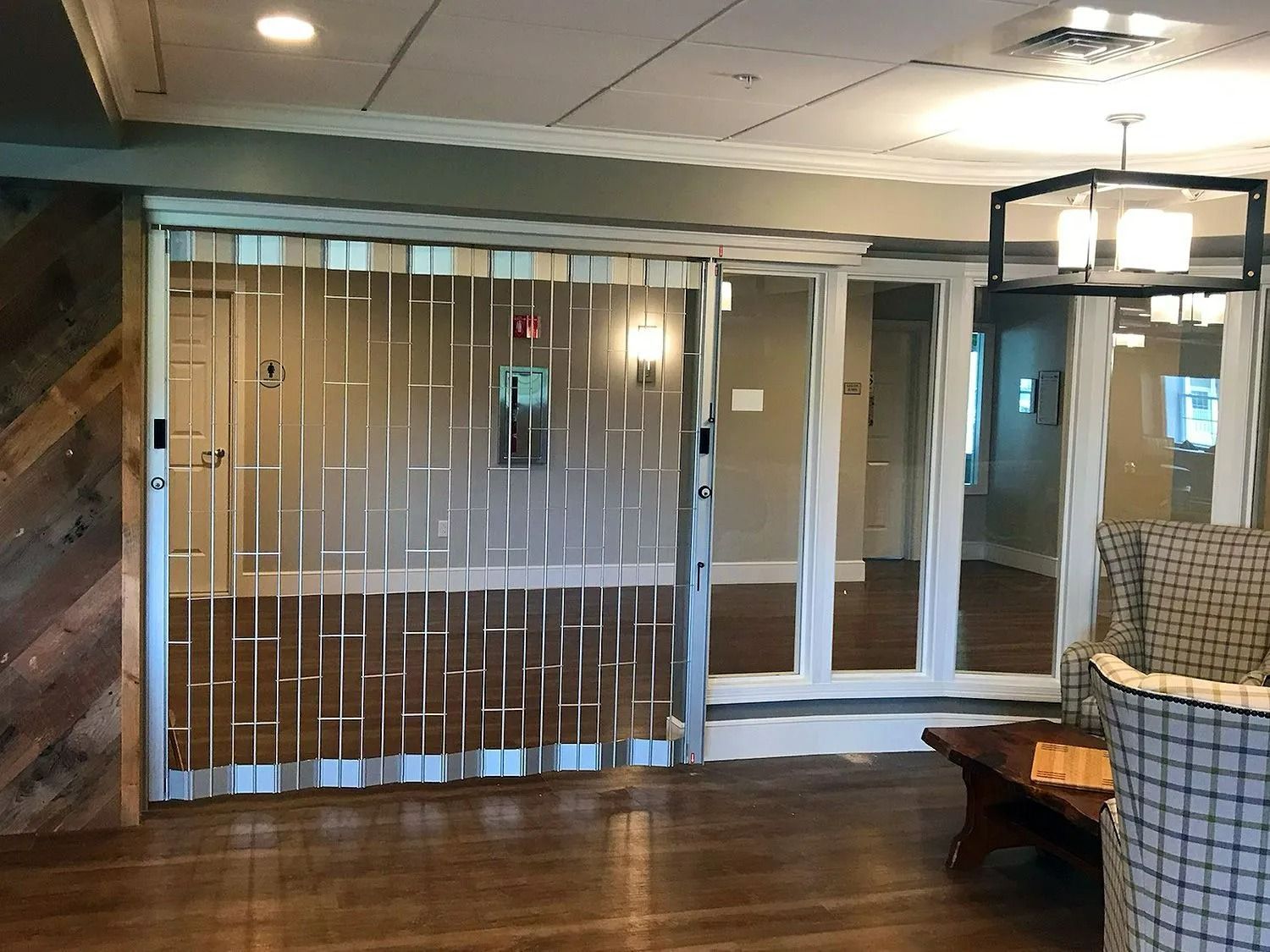 Hotel lobby with glass doors, wood paneling, and a seating area under warm ceiling lights
