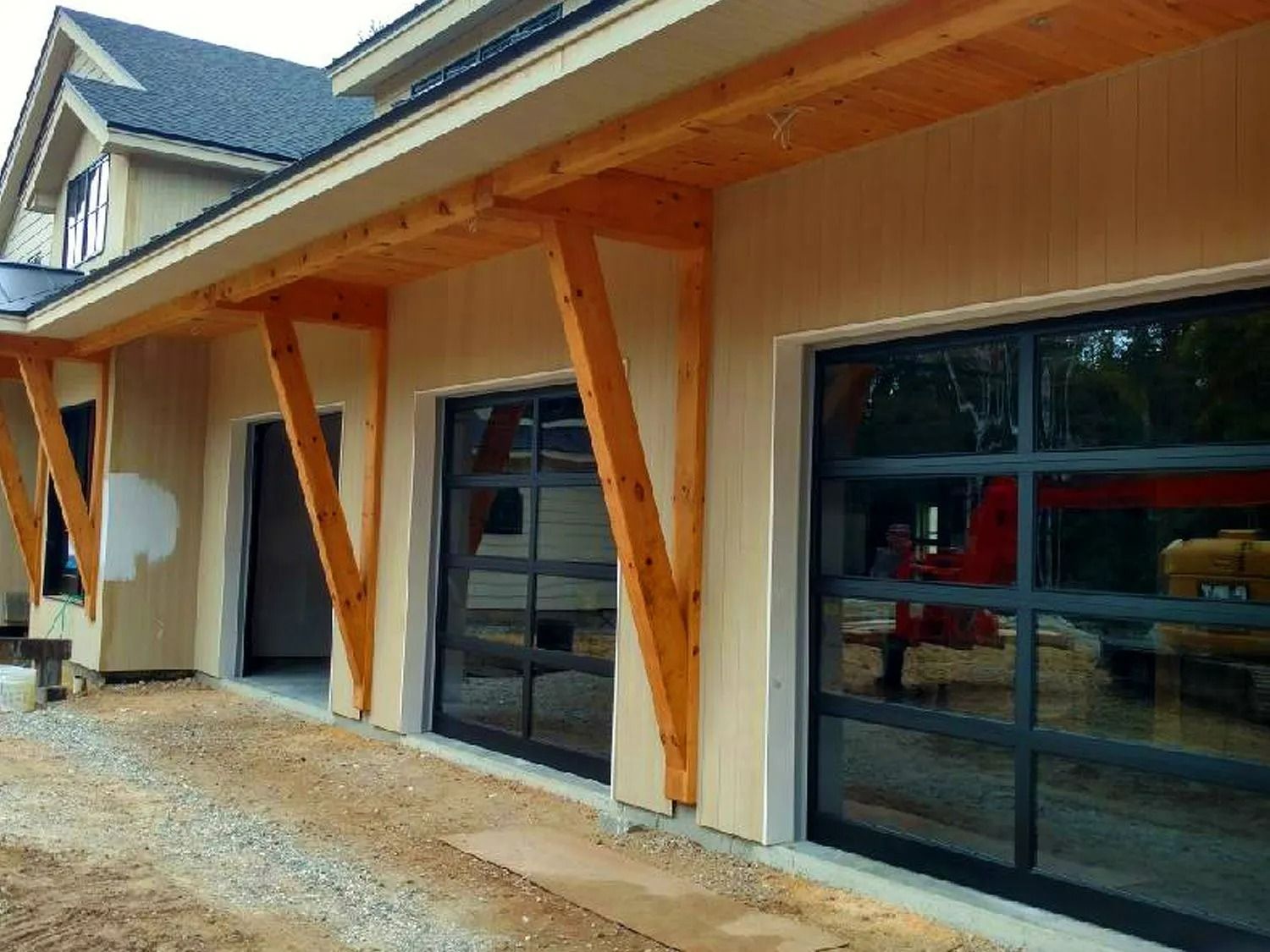 Exterior of a building with wood posts, a covered porch, and large black-framed windows above gravel.