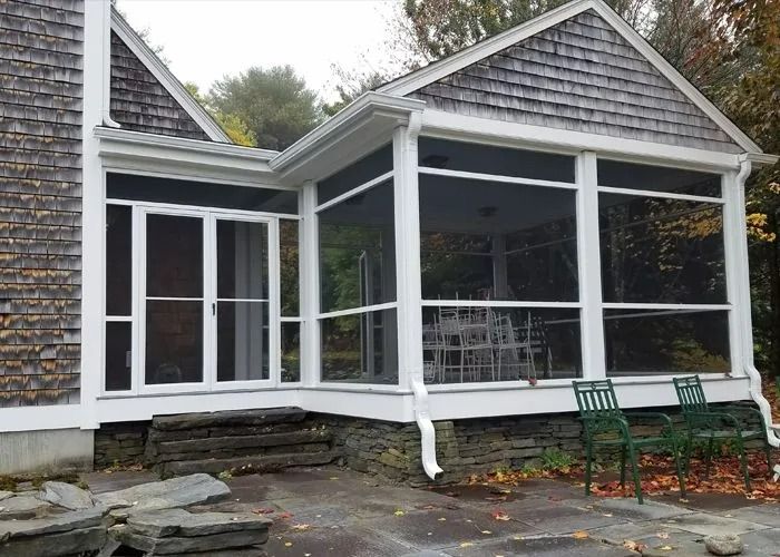 House with screened porch and white trim, stone steps, and green chairs on a wet patio