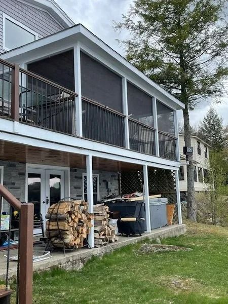 Screened porch on a house with stacked firewood, bins, and a grassy yard below