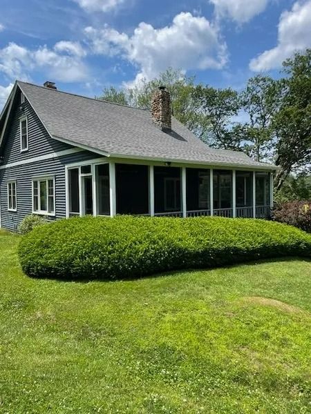 Gray house with a screened porch, white trim, and a manicured hedge under a blue sky