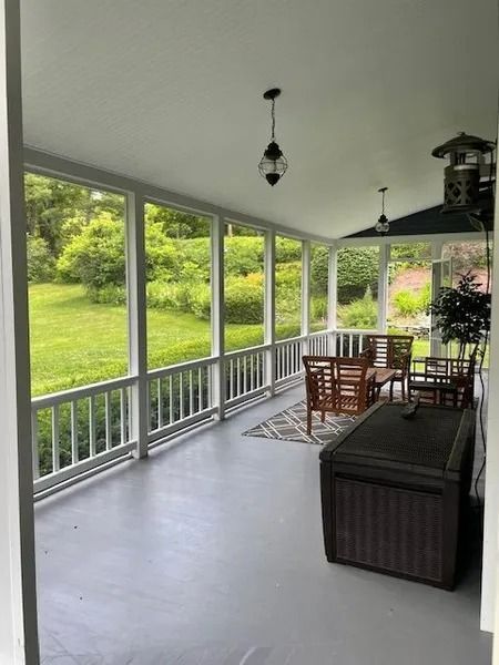 Covered porch with wicker seating, dining table, and large windows overlooking a green lawn