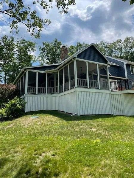 Blue house with a screened porch and white skirting on a grassy hill under a cloudy sky