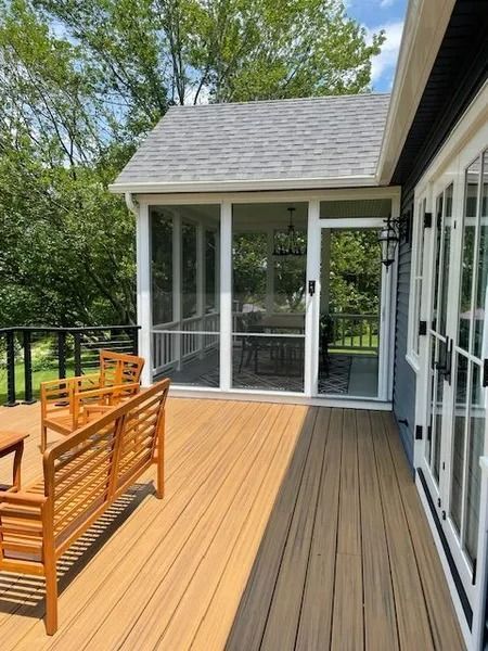 Wooden deck with benches and a screened porch beside a modern house, surrounded by trees