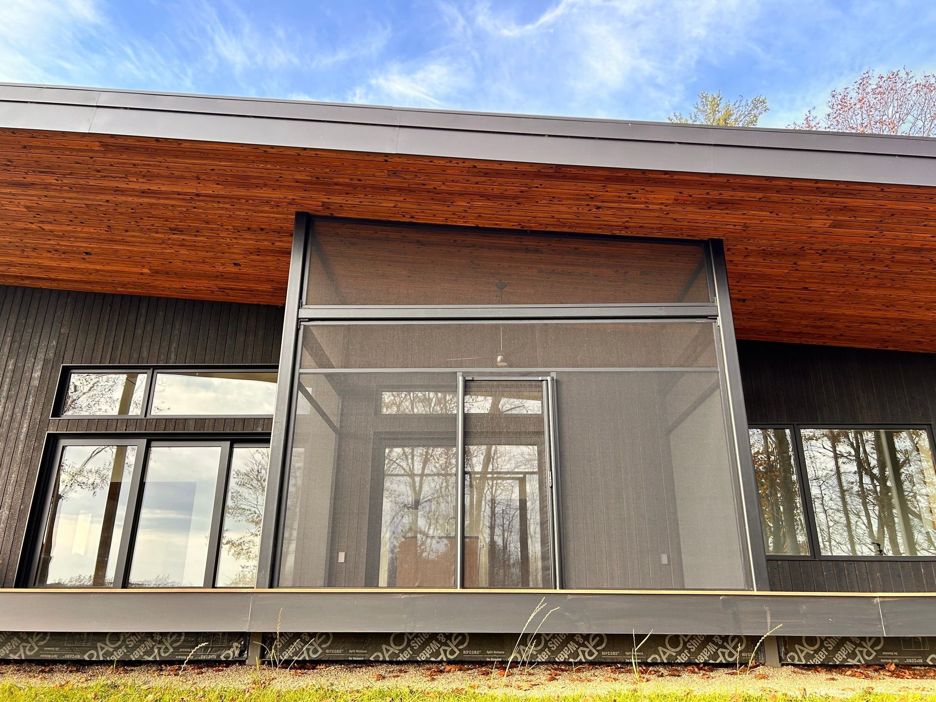 Modern house facade with a screened-in porch and large windows under a wooden roofline