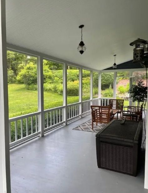 Screened porch with white railing, wicker furniture, and green lawn view through large windows