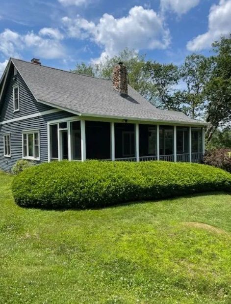 Gray house with white trim, screened porch, and manicured green lawn under a partly cloudy sky