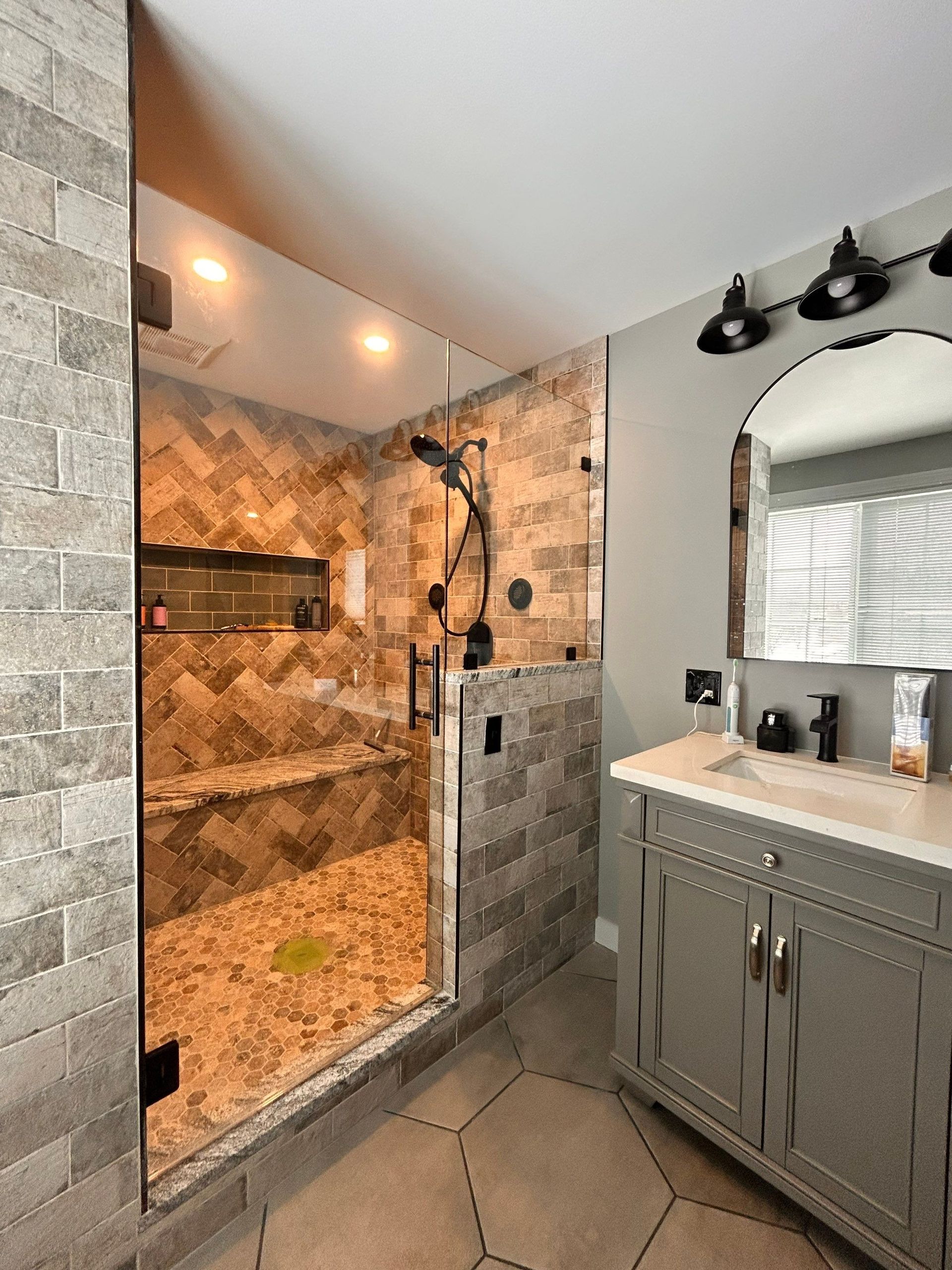 Modern bathroom with tiled walk-in shower, glass door, and gray vanity sink.