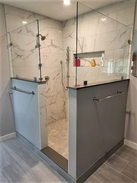 Modern glass shower enclosure with marble-look tile and gray vanities in a bathroom