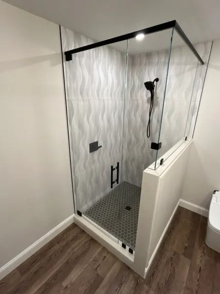 Modern glass walk-in shower with black fixtures, tiled floor, and white half wall in a bathroom
