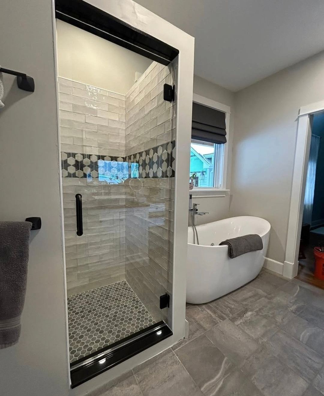 Modern bathroom with glass shower, mosaic tile, and freestanding tub by a window