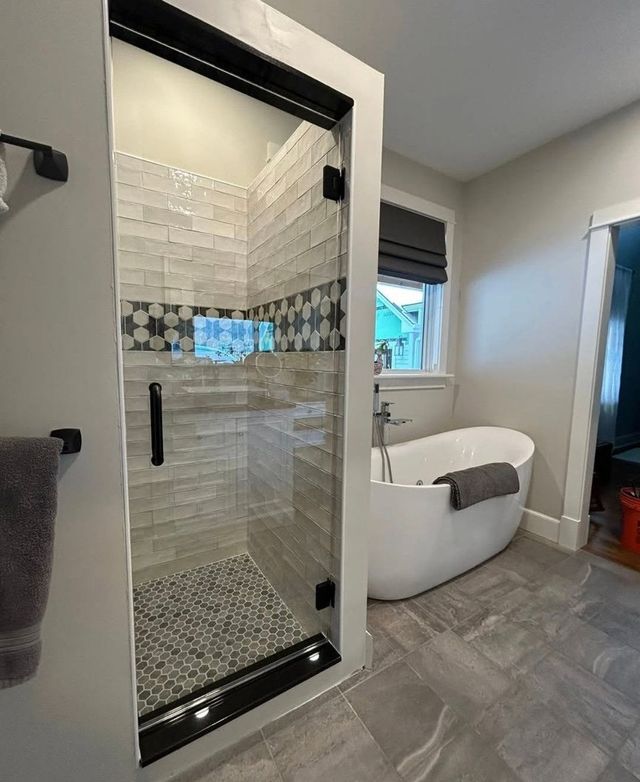 Modern bathroom with glass shower, freestanding tub, and gray tile flooring