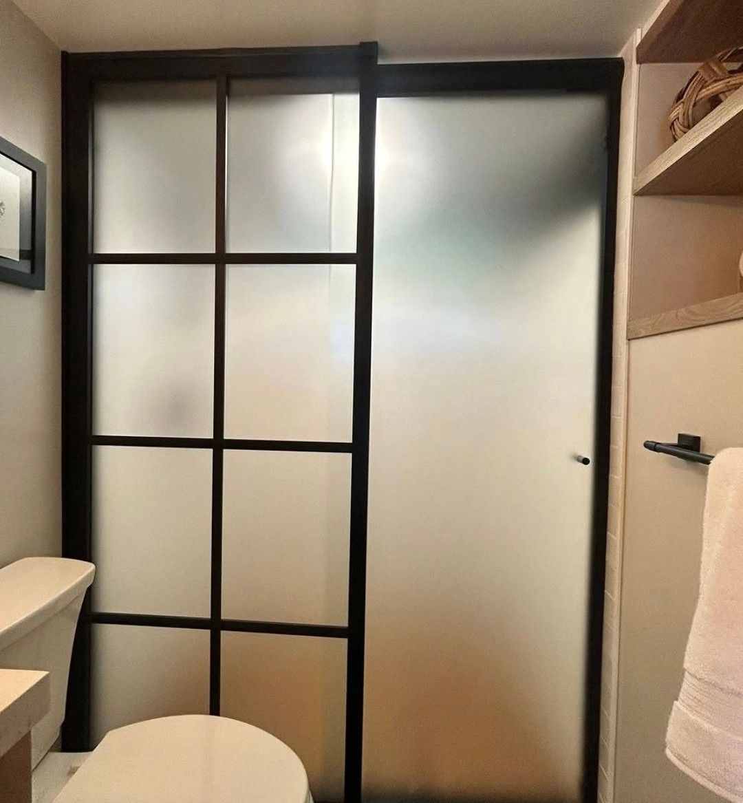 Small bathroom with frosted glass shower door, black-framed panel, and towel on a hook
