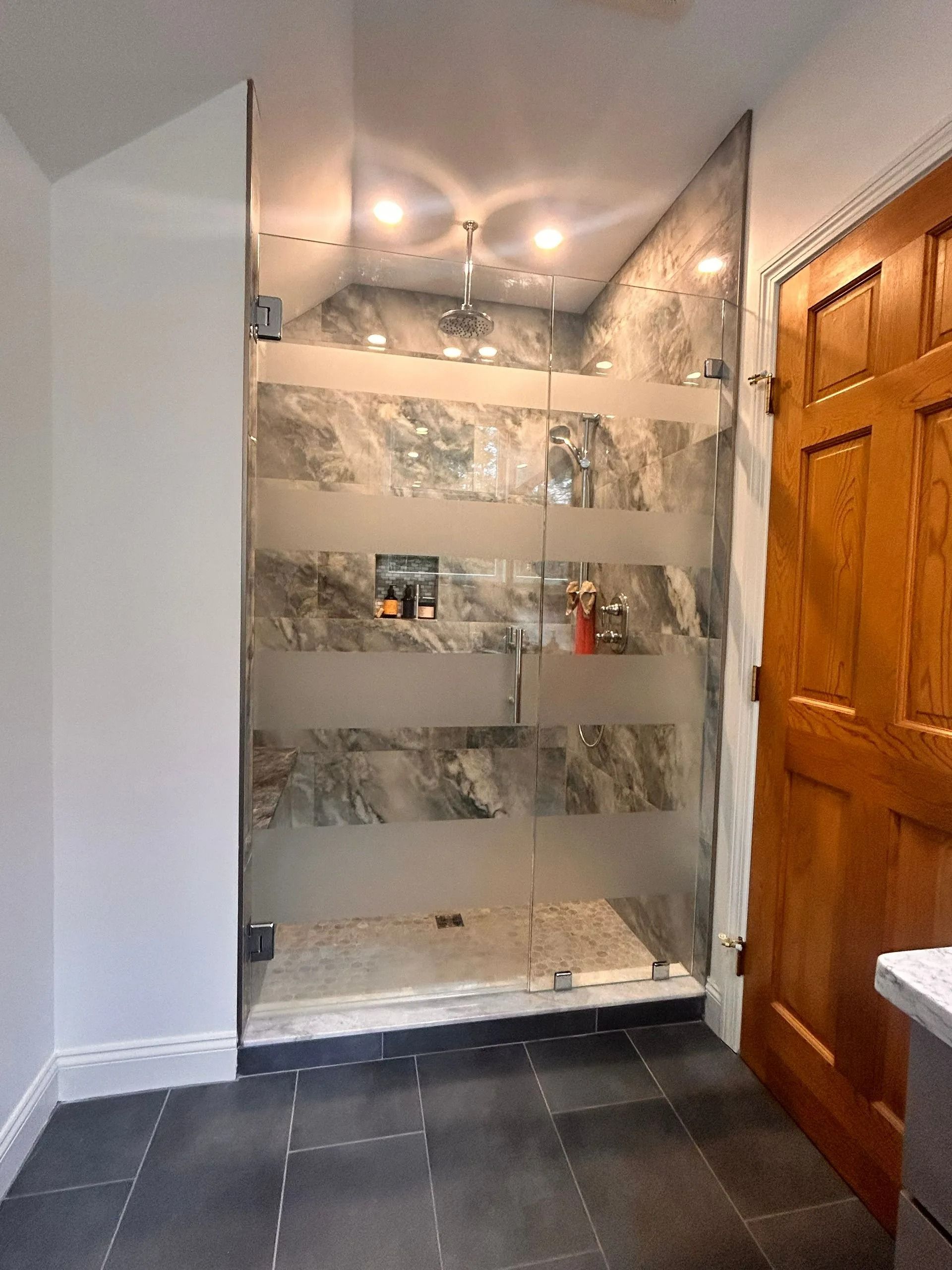 Bathroom with tiled shower niche, glass doors, and a wooden door beside a tiled floor.