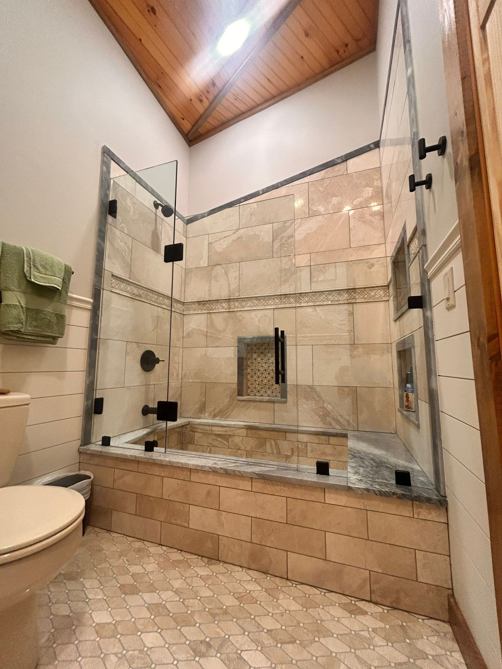 Spacious beige tiled bathroom with glass shower, soaking tub, and sloped wood ceiling