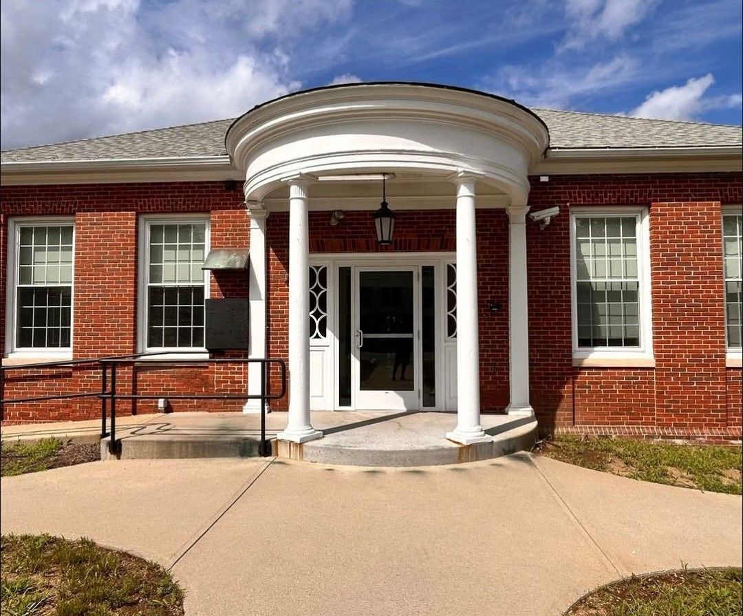 Front entrance of a red brick building with white columns, windows, and a curved porch roof