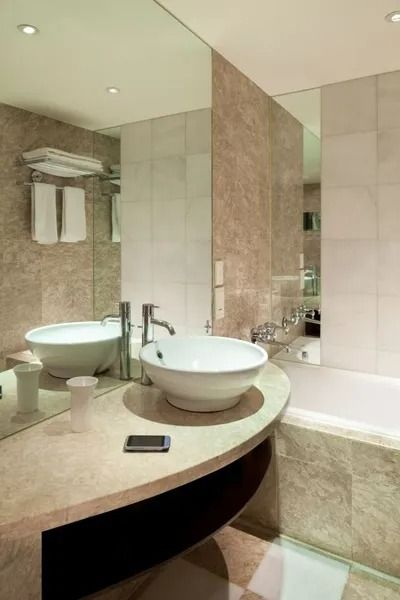 Modern bathroom with a curved vanity, two vessel sinks, mirror, and beige tile shower area