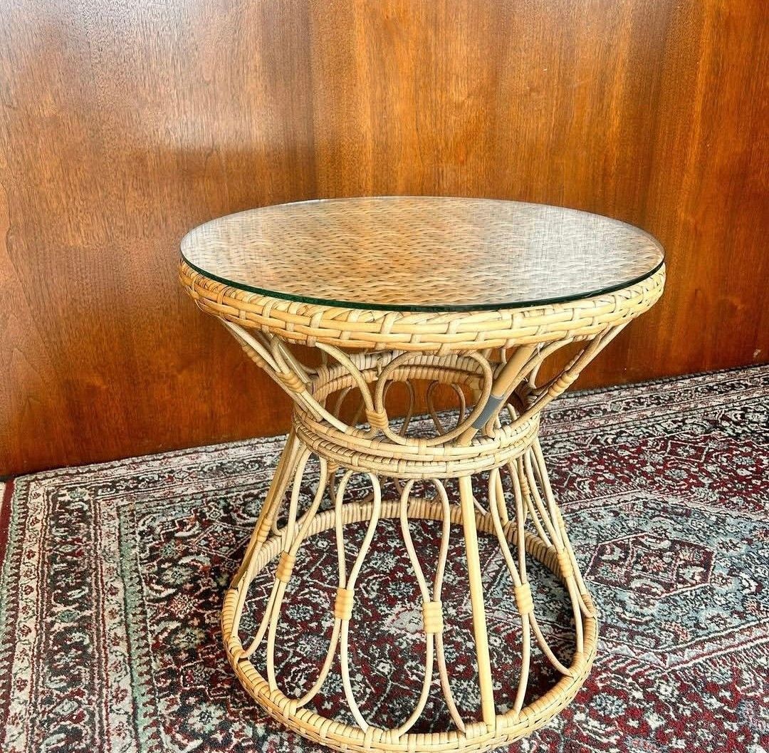 Round wicker table with glass top on a patterned rug against a wood-paneled wall