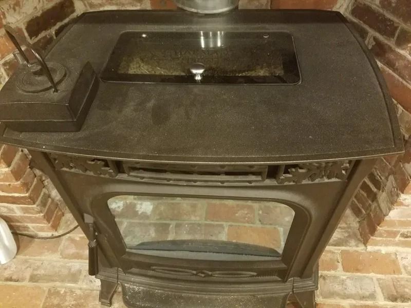 Black cast-iron wood stove with glass top and lower firebox, set against a brick wall