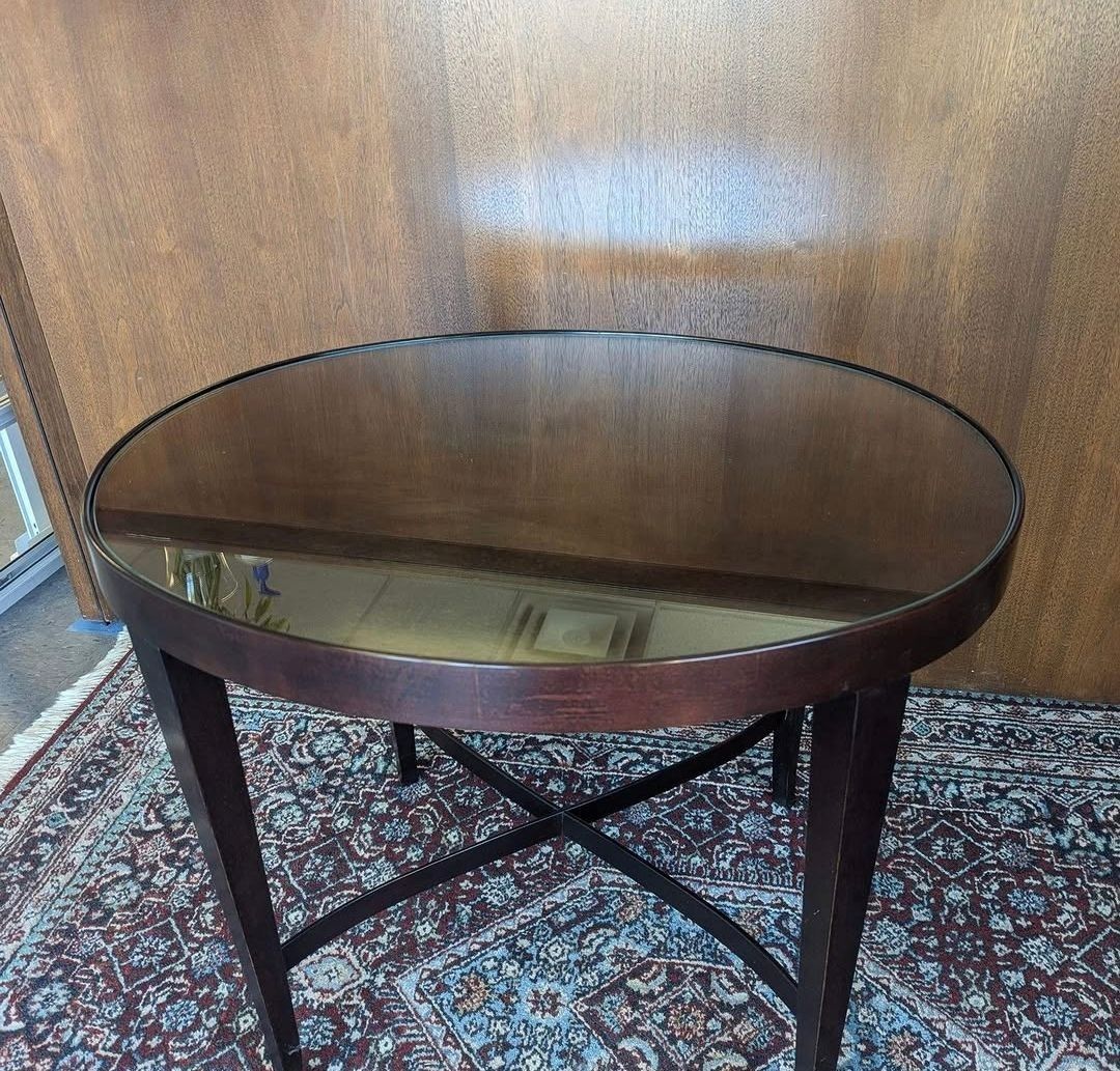 Round dark wood table with a glass top on a patterned rug, against a wood-paneled wall
