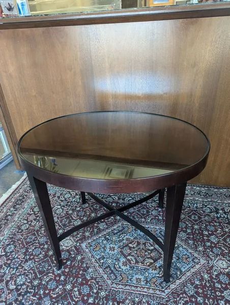 Round dark wood table with a reflective top on a patterned rug against a wood-paneled wall