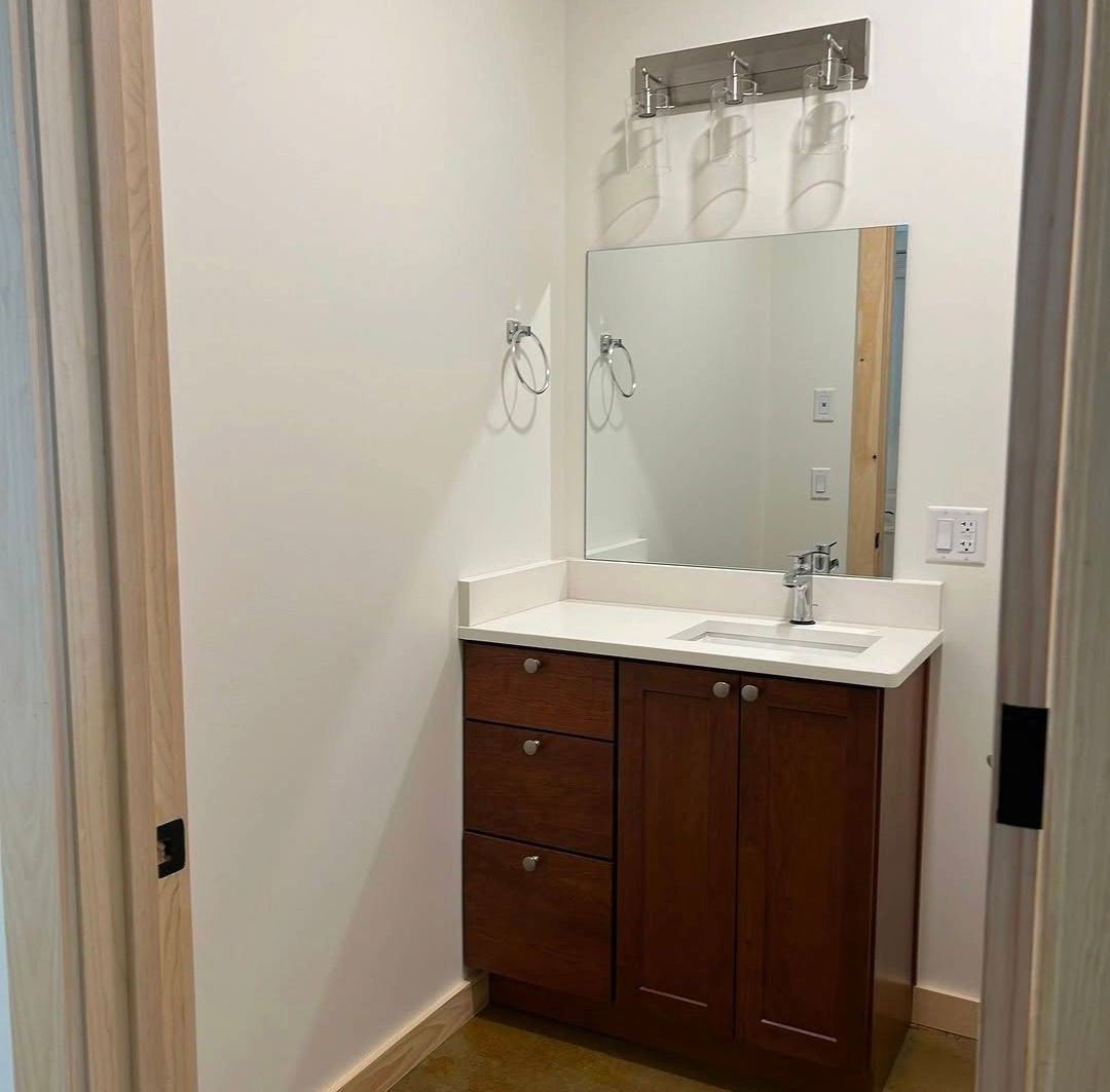 Bathroom vanity with mirror, white sink, and dark wood cabinet in a narrow room.