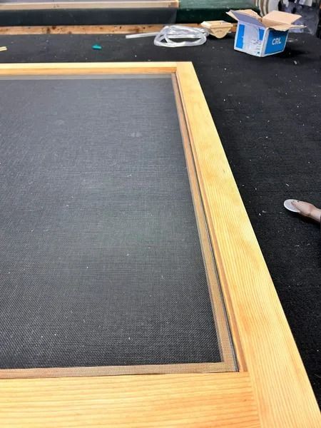 Wooden frame on a dark work surface with tools and a small box in the background.