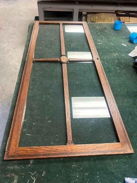 Wooden framed glass cabinet door with four panes, lying on a green surface outdoors.