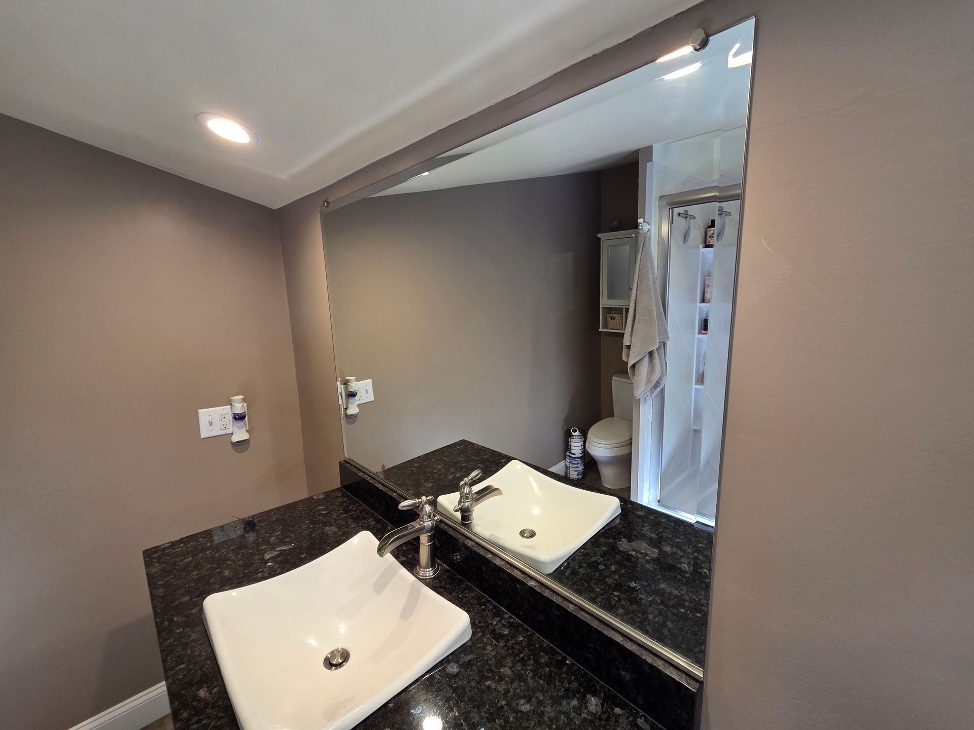 Modern bathroom vanity with white sink, black countertop, and large mirror reflecting a shower area