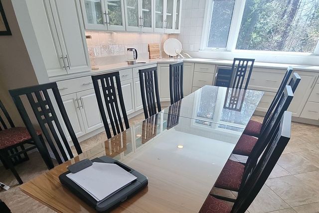 Dining table with several chairs and a tray near a bright kitchen window