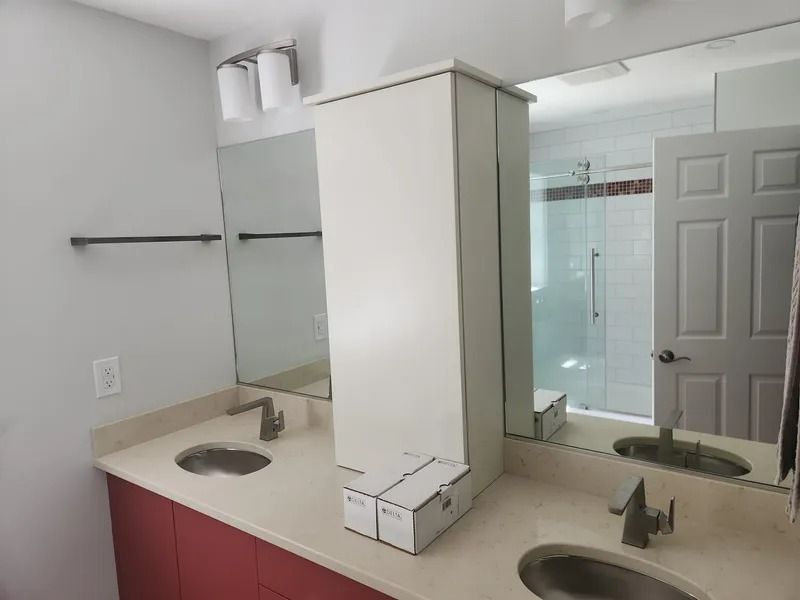 Bathroom vanity with double sinks, mirrors, and a glass shower in the background