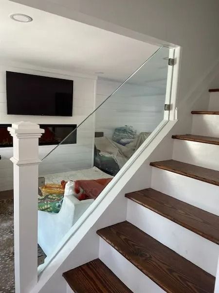 Staircase beside a glass railing overlooking a bright living room with a wall-mounted TV and sofa.